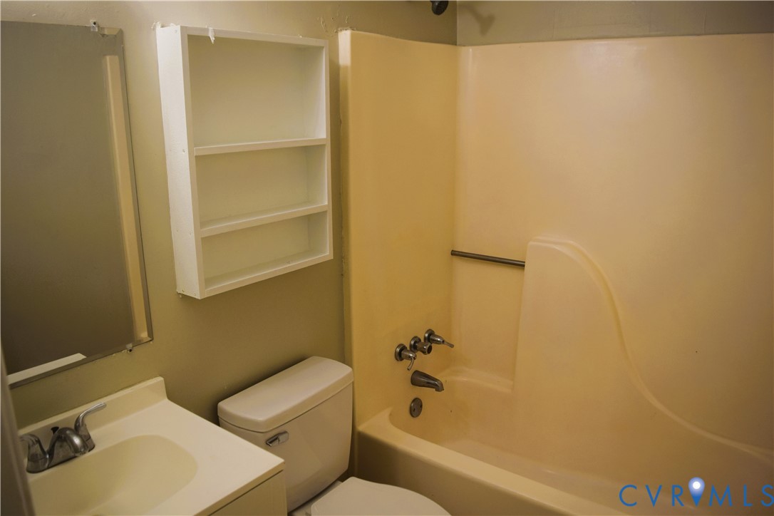 Full bathroom featuring a molded composite tub and shower surround, wall-mounted storage cabinetry, vanity with integrated basin, and polished chrome plumbing fixtures
