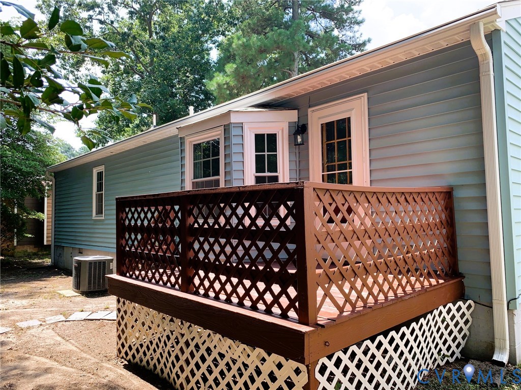 Raised wood deck featuring lattice railing, bay window, light blue horizontal siding, and external light fixture