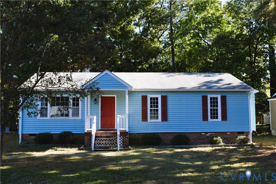 Single-story exterior featuring light blue horizontal siding, a red front door, brick foundation skirting, shuttered windows, and a covered front porch with white railing