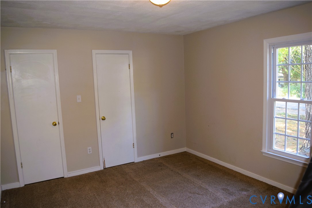 Neutral-toned interior room featuring wall-to-wall carpeting, two interior doors, and a multi-pane window with white trim