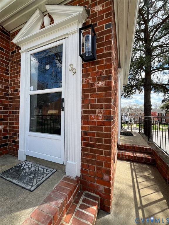 Red brick exterior featuring a white pilaster-framed entryway with a pediment, concrete steps with brick edging, and a black metal exterior sconce