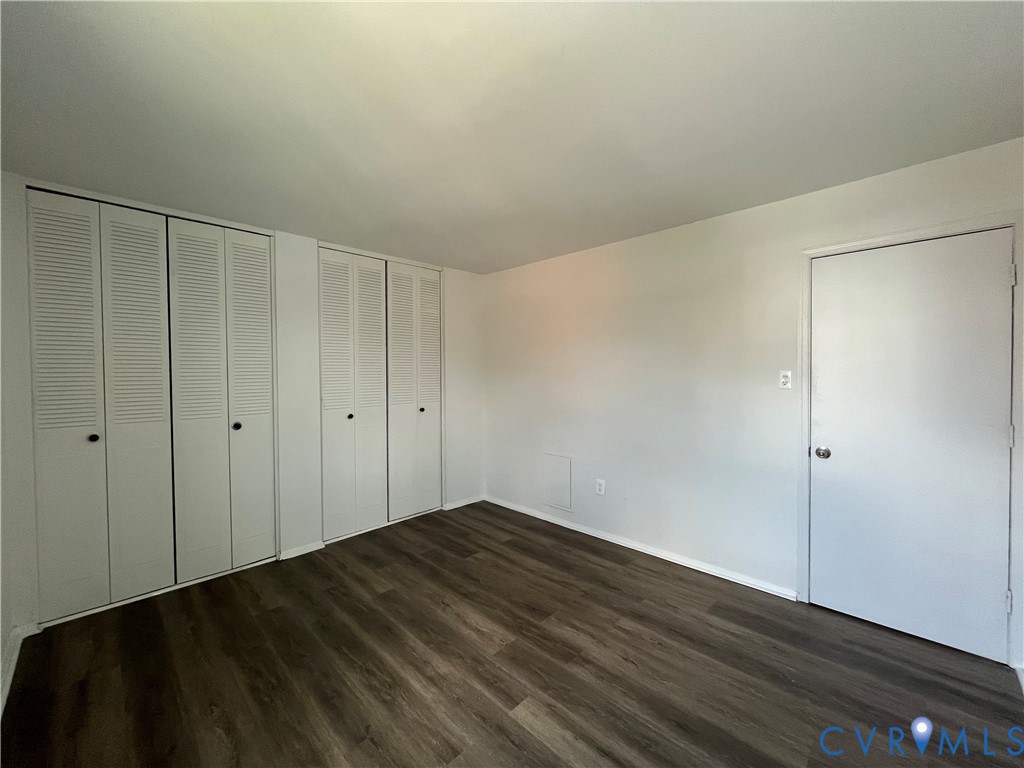 Neutral-toned interior space featuring wood-finish flooring and two sets of built-in louvered-door closets