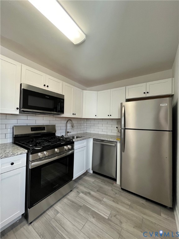 Kitchen featuring white cabinetry, stone-surface countertops, subway tile backsplash, stainless steel appliances, and wood-finish flooring