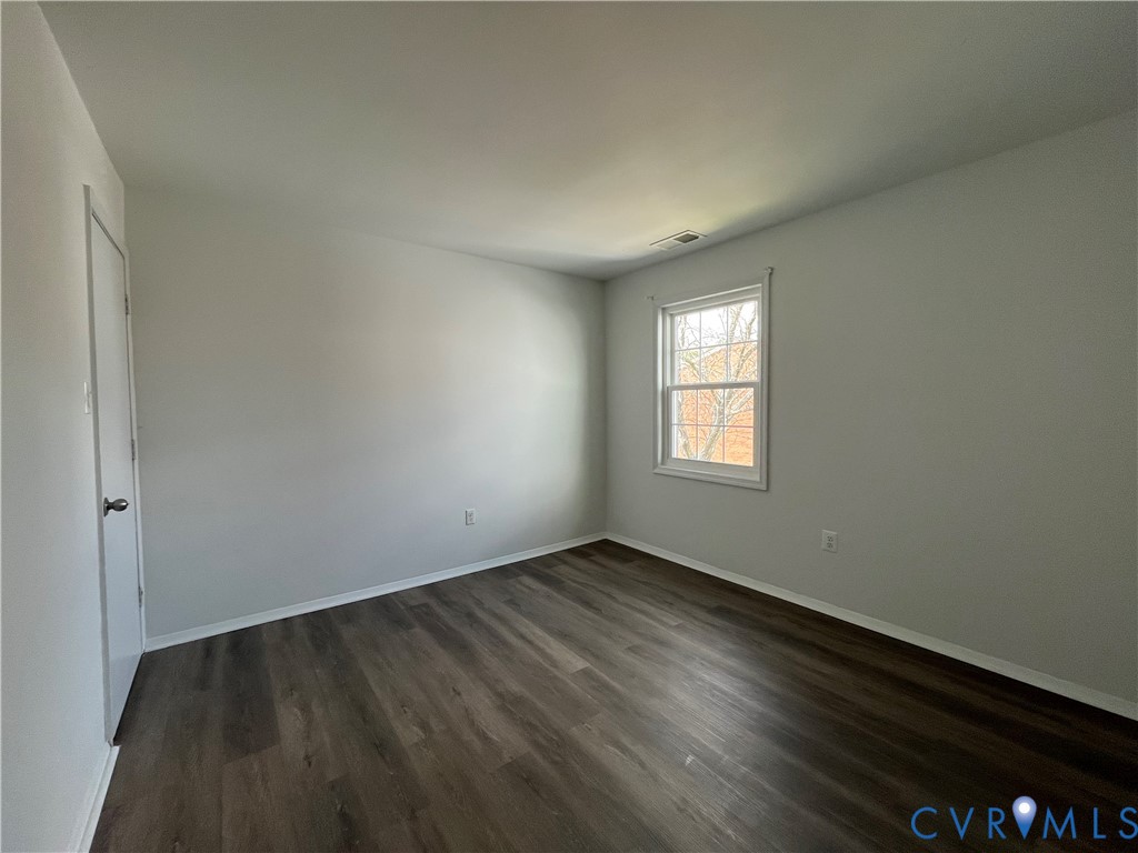 Neutral-toned interior space featuring wood-finish flooring, a single-hung window with a grille pattern, and a hinged closet door