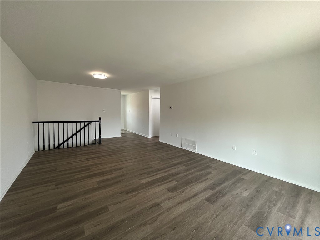 Open-concept interior featuring wood-finish flooring, neutral walls, and a black metal staircase railing