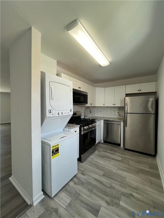 Kitchen featuring white cabinetry, stone-finish countertops, subway tile backsplash, wood-finish flooring, and stainless steel appliances