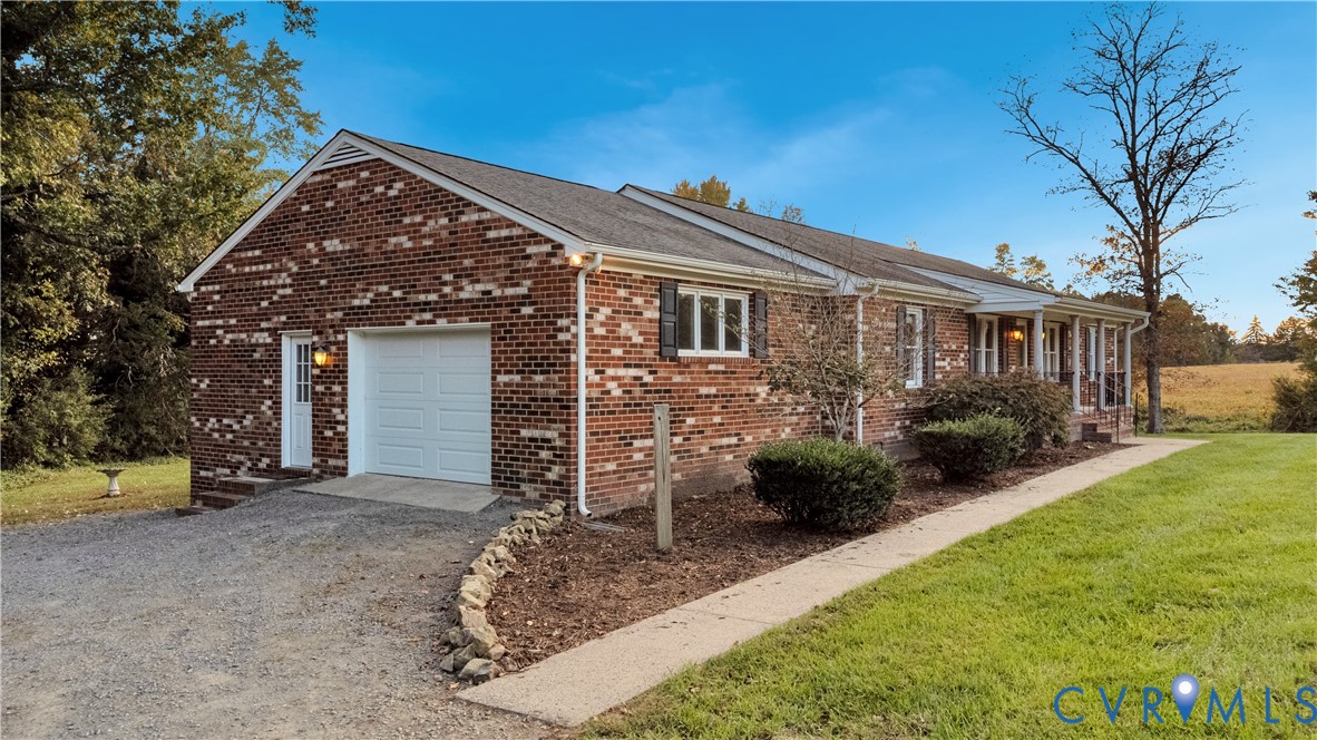 Multi-tone brick exterior featuring a shingle roof, attached garage with sectional door, and a concrete walkway