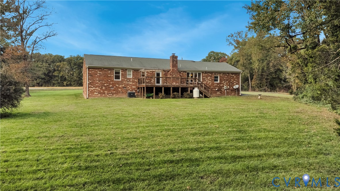 Brick exterior residence featuring a raised wood deck, a prominent masonry chimney, and expansive grounds