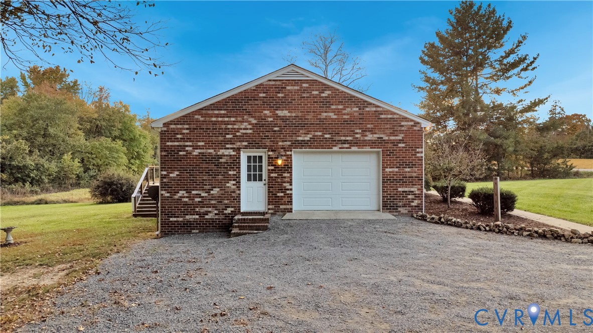 Detached brick garage featuring a single-car overhead door, a pedestrian service door, and a gravel driveway