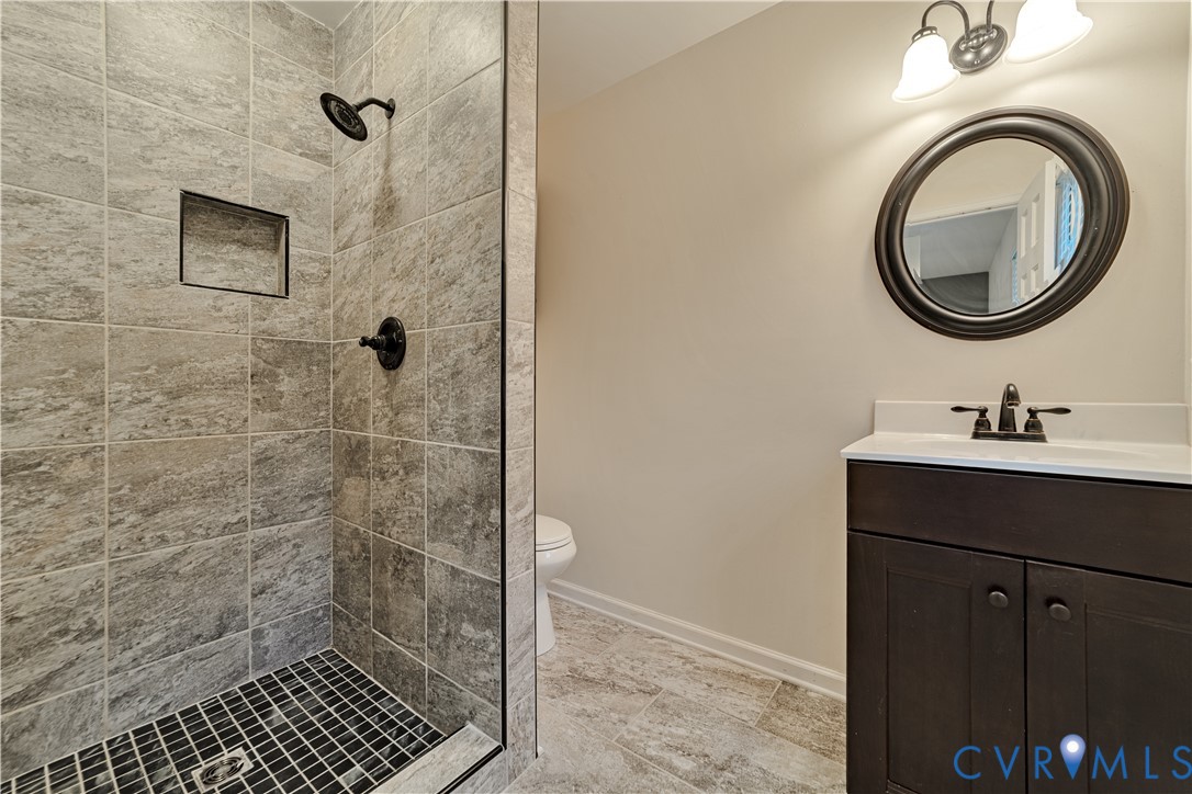 Walk-in shower with textured tile surround, built-in wall niche, and matte black hardware, paired with a dark wood-finish vanity and integrated vanity lighting