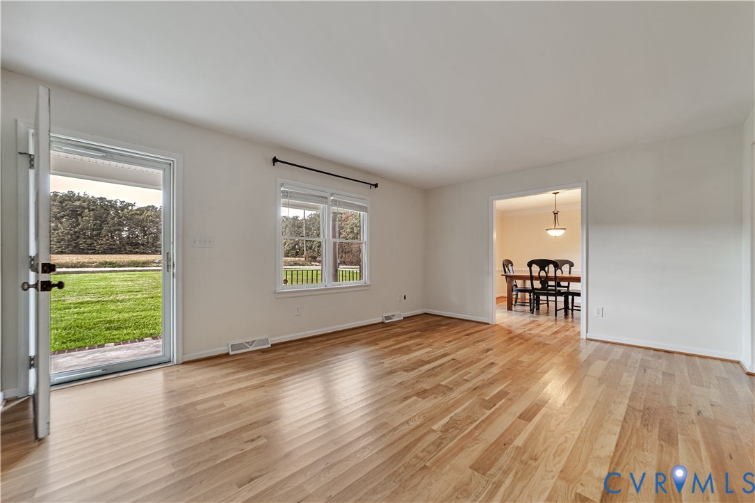 Light-filled room featuring wood-finish flooring, a glass-paneled exterior door, and double-hung windows Light-filled room featuring wood-finish flooring, a glass-paneled exterior door, and double-hung windows