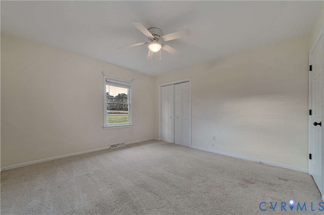 Neutral interior featuring wall-to-wall carpeting, a ceiling fan with integrated lighting, and dual-panel closet doors