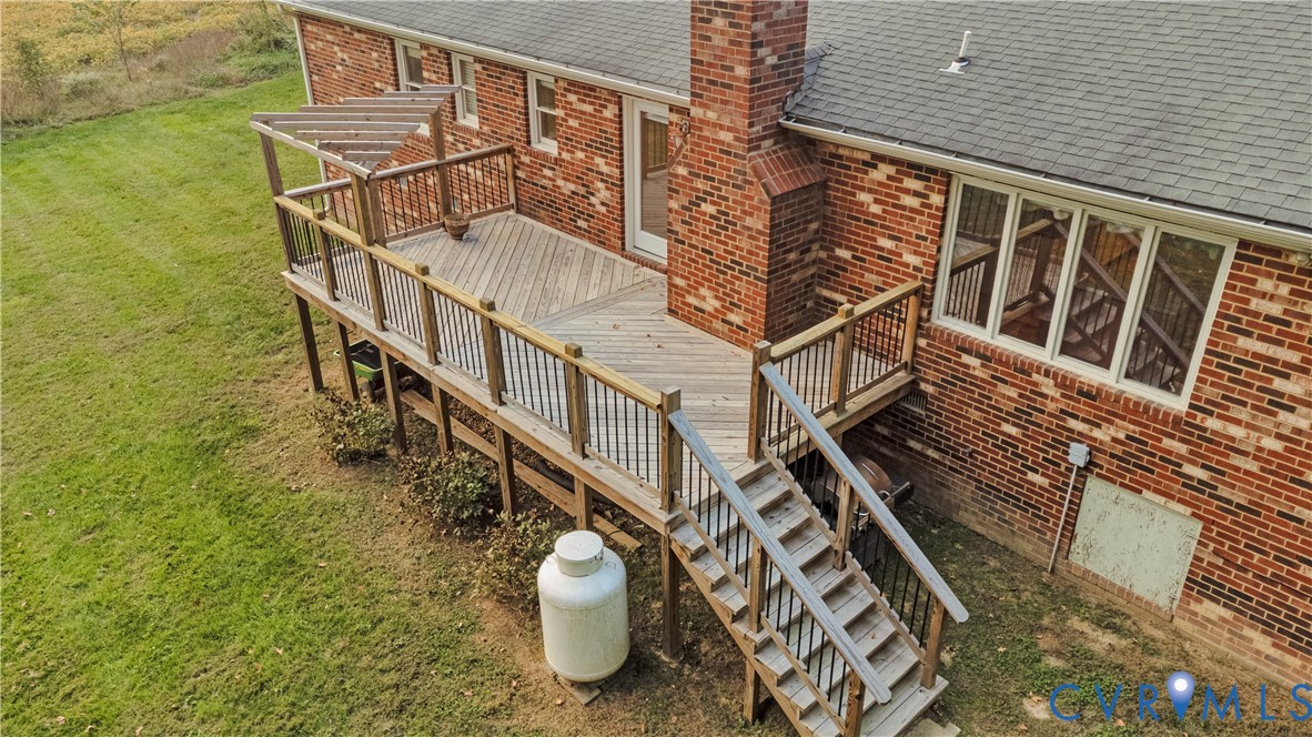 Multi-level exterior featuring a red brick facade, an elevated wood deck with a diagonal pattern floor, a built-in pergola, and a masonry chimney