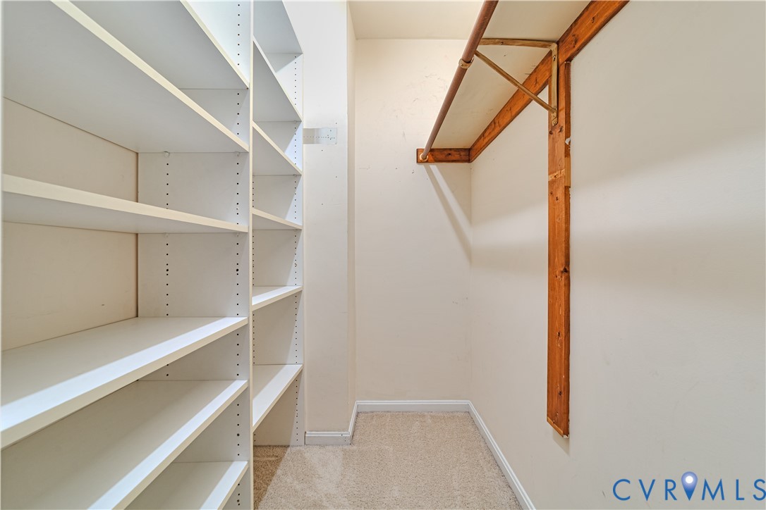 Storage space featuring custom white shelving units and a wooden hanging rod with a bracketed shelf
