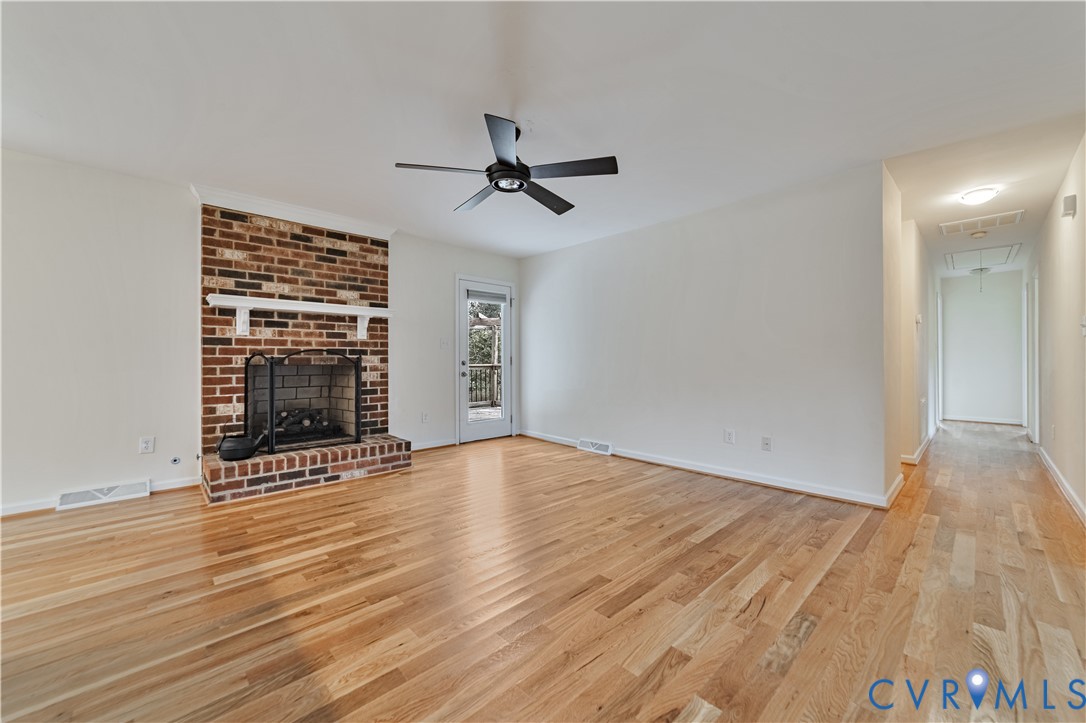 Open living area featuring wood-finish flooring, a full-height brick fireplace with a white mantel, and a black ceiling fan