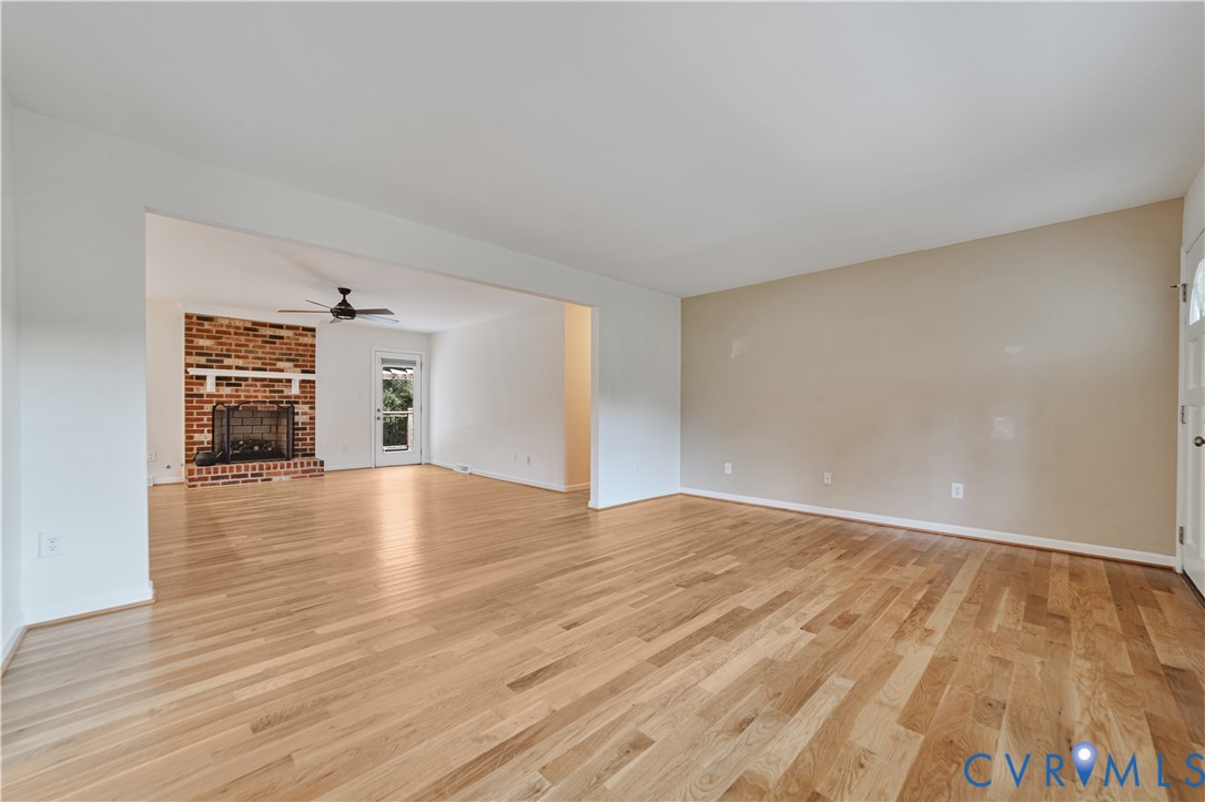 Living area featuring light wood-finish flooring, masonry fireplace with a white mantel, ceiling fan, and entry door with glass paneling Living area featuring light wood-finish flooring, masonry fireplace with a white mantel, ceiling fan, and entry door with glass paneling