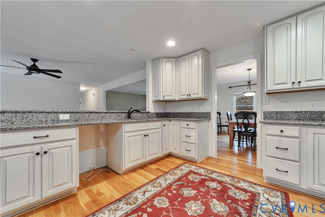 Kitchen featuring white cabinetry, stone-surface countertops, wood-finish flooring, and a ceiling-mounted fan