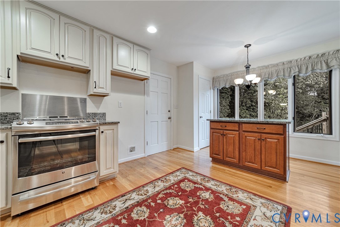 Kitchen featuring light-toned cabinetry, stainless steel gas range, stone-surface countertops, wood-finish flooring, and a free-standing wooden island