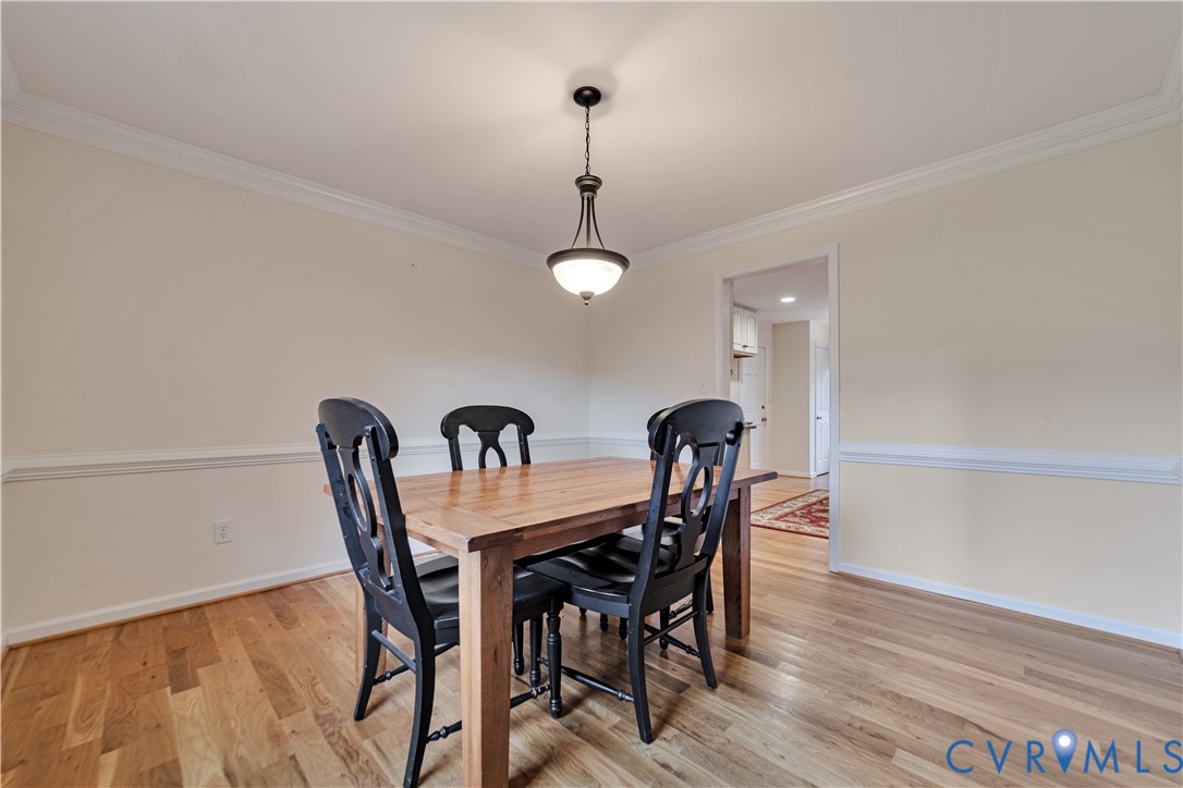Room featuring wood-finish flooring, chair rail molding, crown molding, and a suspended metal pendant light fixture