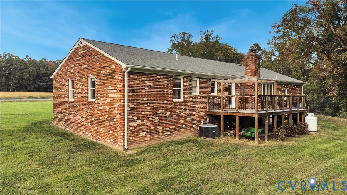 Brick exterior residence featuring a raised wooden deck with a pergola, a brick chimney, and an expansive lawn