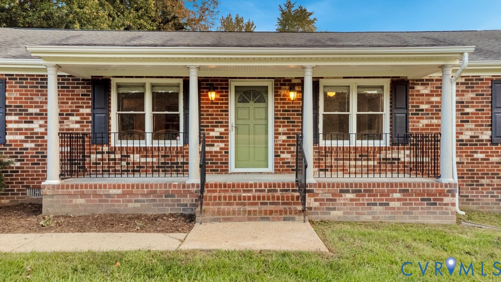 Brick exterior featuring a covered front porch with round columns, black wrought iron railing, and a central entryway Brick exterior featuring a covered front porch with round columns, black wrought iron railing, and a central entryway