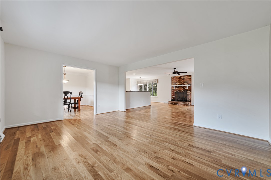 Open-concept interior featuring wood-finish flooring, a full-height brick masonry fireplace with a white mantel, and ceiling-mounted fans Open-concept interior featuring wood-finish flooring, a full-height brick masonry fireplace with a white mantel, and ceiling-mounted fans