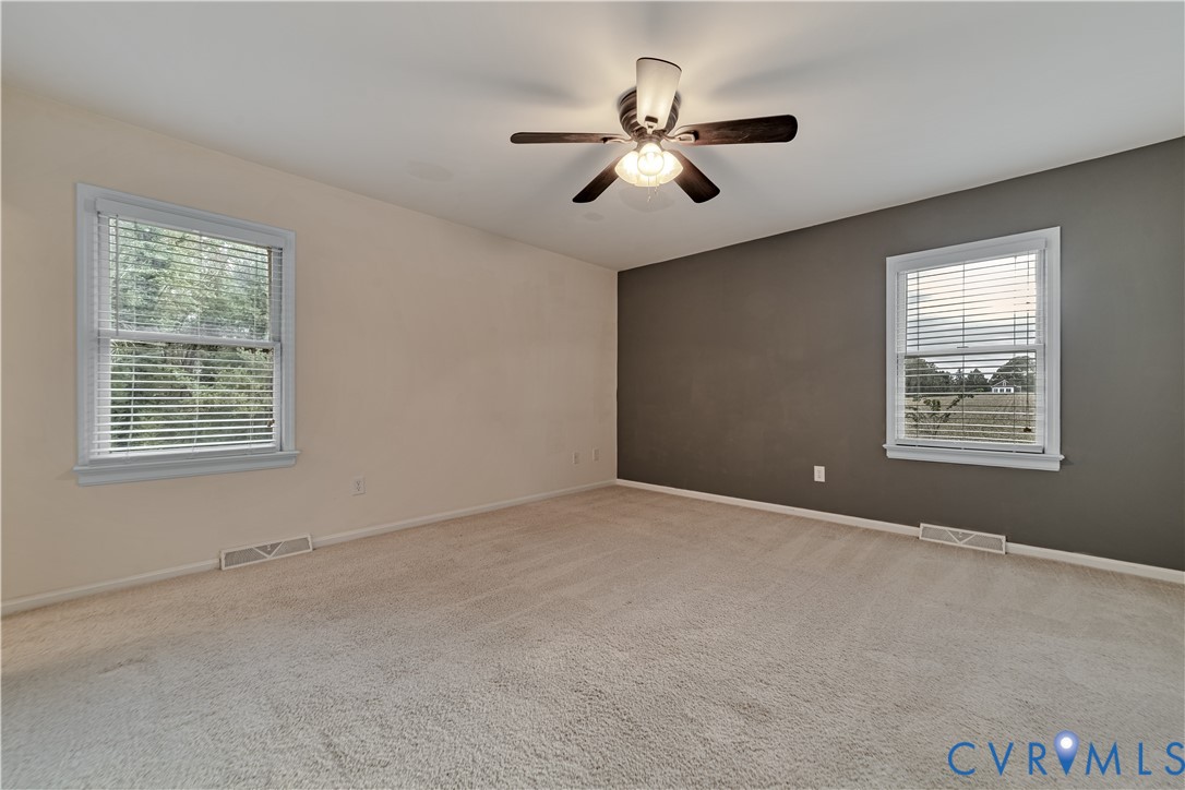 Neutral-toned carpeted room featuring dual-tone painted walls, two windows with blinds, and a central ceiling fan with an integrated light fixture
