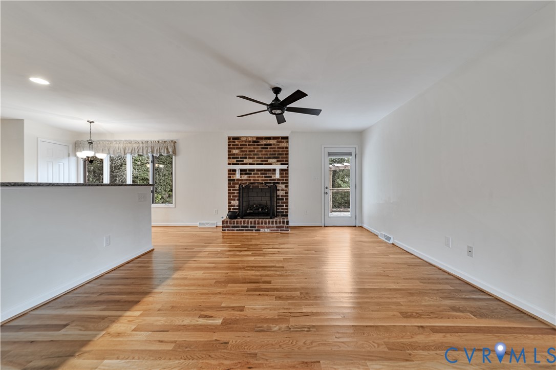Living area featuring wood-finish flooring, a brick fireplace with a mantel, a ceiling fan, and a glass-paneled exterior door Living area featuring wood-finish flooring, a brick fireplace with a mantel, a ceiling fan, and a glass-paneled exterior door