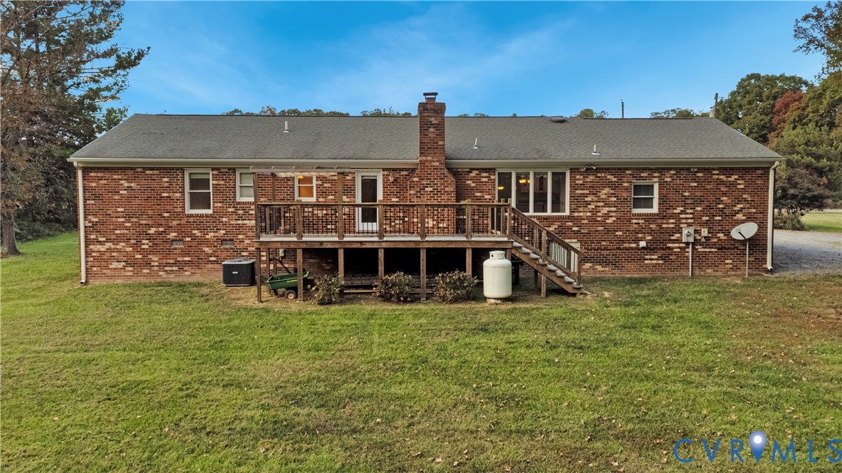 Brick exterior residence featuring a raised wooden deck with railings, a centered masonry chimney, and multi-pane windows