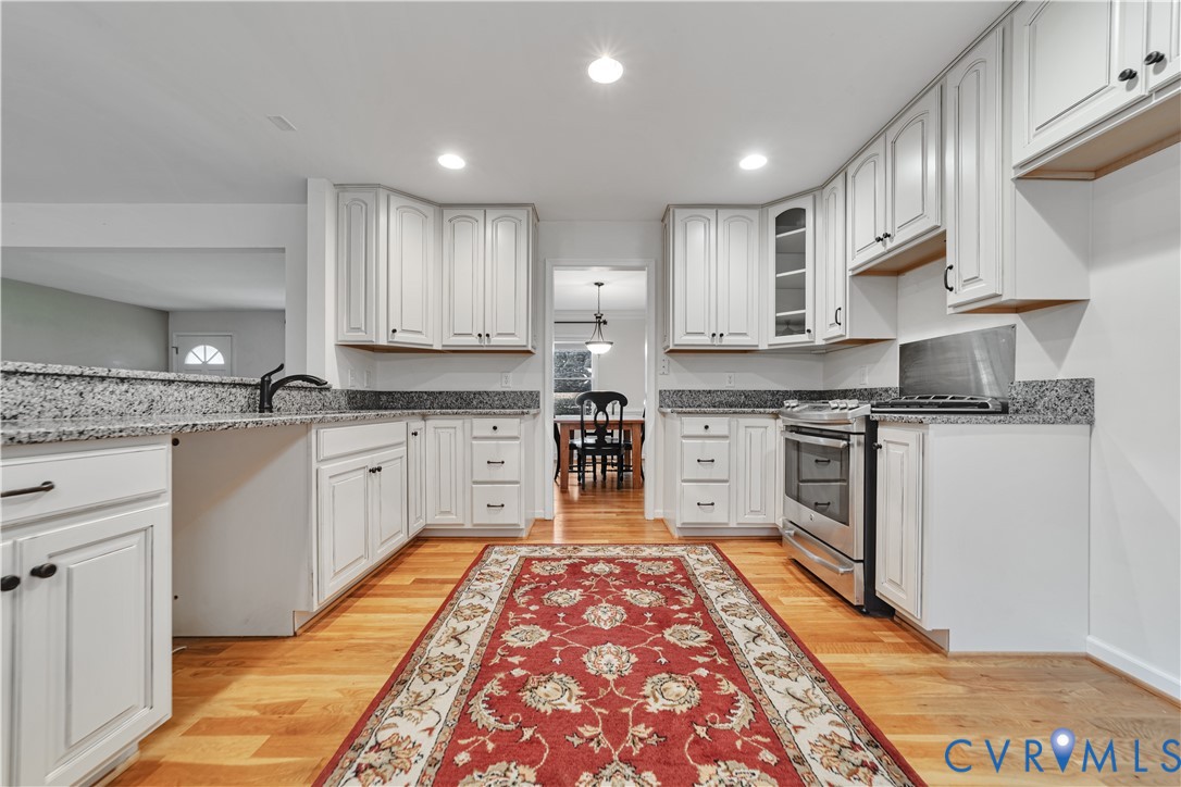 Kitchen featuring white shaker-style cabinetry, stone-surface countertops, wood-finish flooring, and stainless steel range
