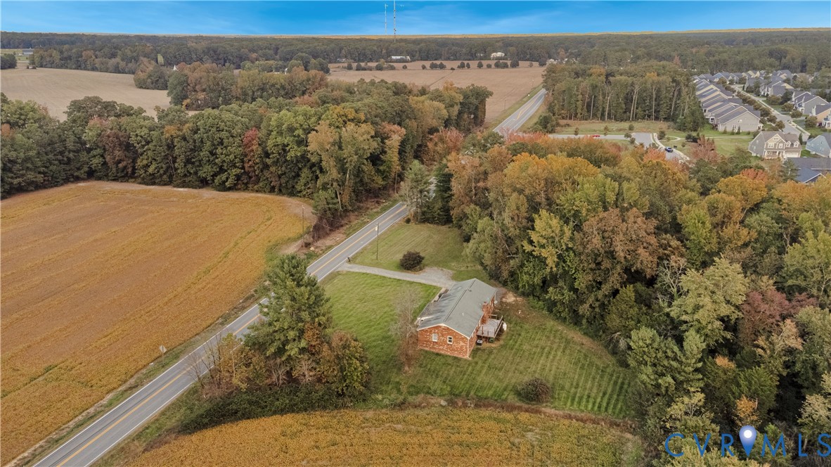 Aerial perspective featuring brick exterior construction, metal roofing, expansive lawn space, and mature perimeter trees