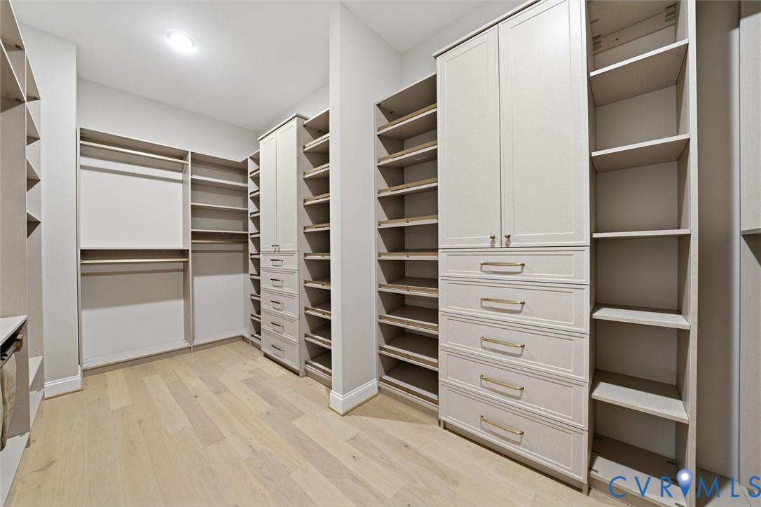 Walk-in closet featuring custom built-in cabinetry, floor-to-ceiling shelving, integrated drawer banks, metallic hardware, and wood-finish flooring