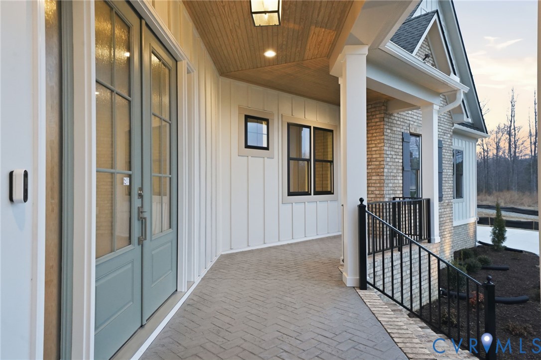 Covered entryway featuring board-and-batten siding, a brick facade, herringbone-patterned brick pavers, a wood-finish ceiling, and double glass-pane doors