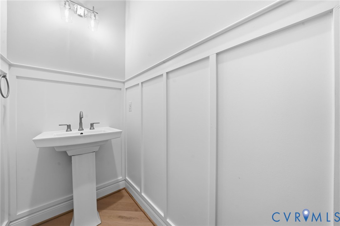 White board-and-batten wall detailing, pedestal sink with chrome faucet, multi-light vanity fixture, and wood-finish flooring