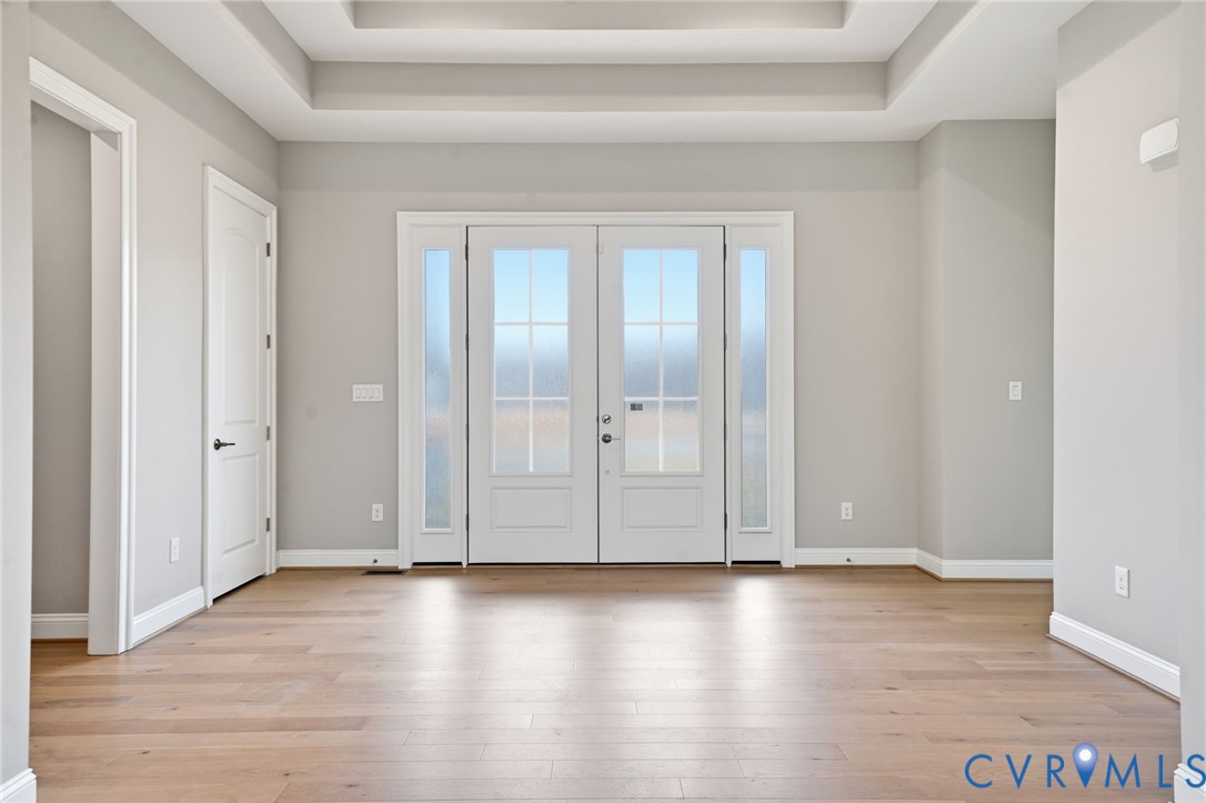 Double entry doors with glass pane inserts and flanking sidelights, complemented by wood-finish flooring and a tray ceiling