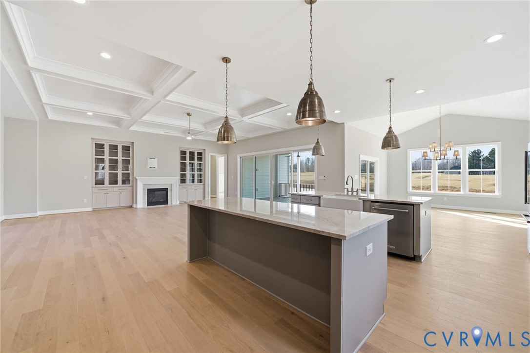 Coffered ceiling, wood-finish flooring, kitchen island with stone countertop, built-in cabinetry with fireplace, and pendant lighting