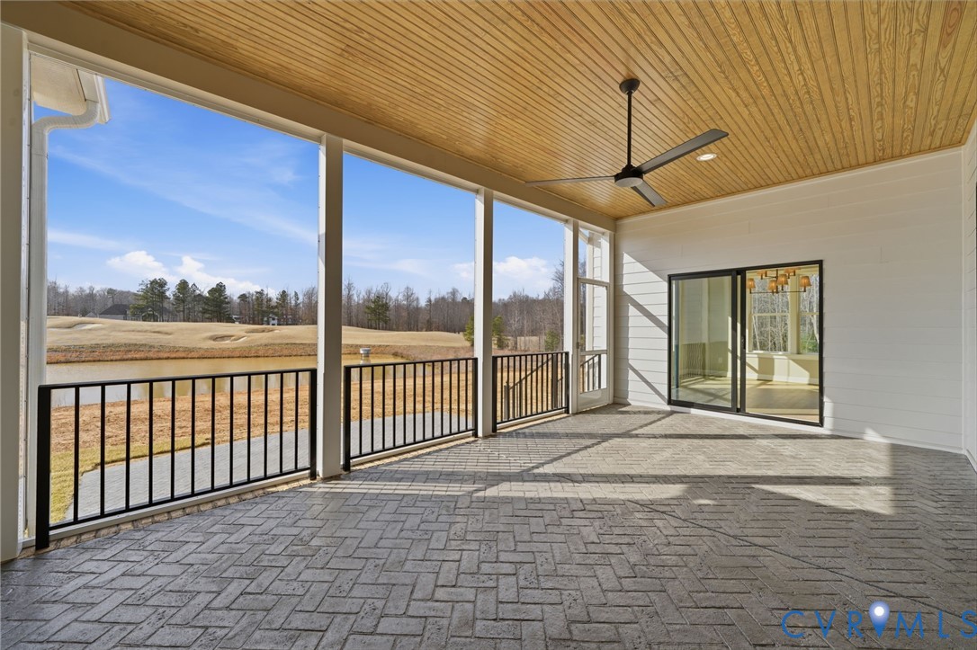 Covered porch featuring a herringbone-patterned paver floor, wood-paneled ceiling, black metal railing, and a ceiling fan