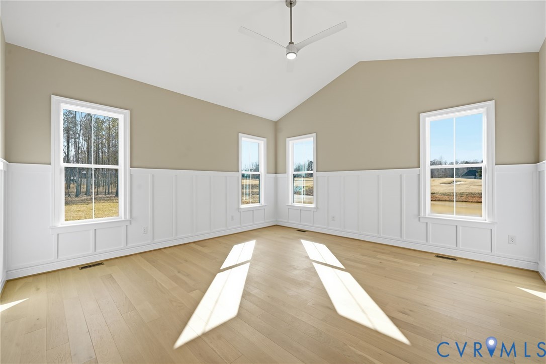 Vaulted ceilings, wood-finish flooring, white board-and-batten wainscoting, and a modern ceiling fan