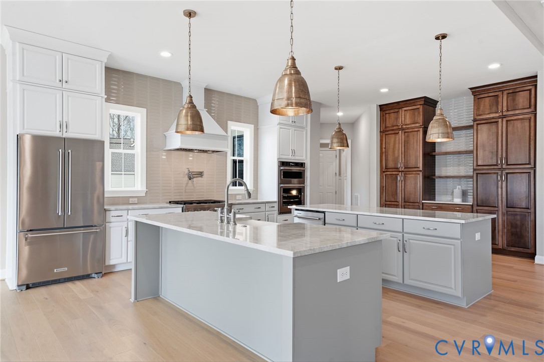 Kitchen featuring a stone-topped central island, stainless steel appliances, built-in double wall ovens, wood-finish cabinetry, and metal pendant lighting