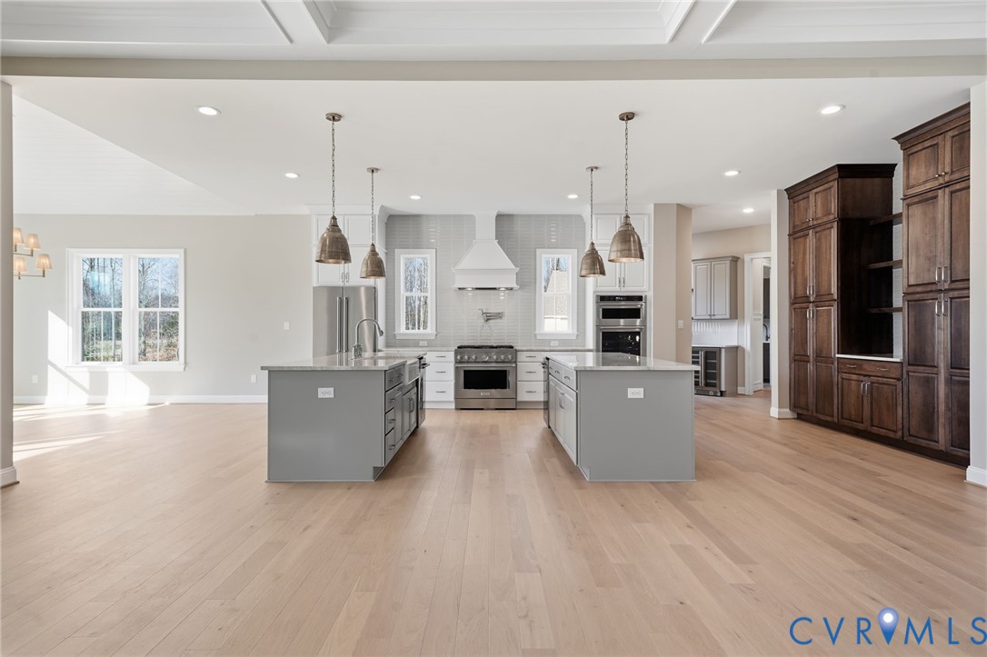Kitchen featuring dual islands with stone countertops, stainless steel appliances, coffered ceiling, and custom wood-finish cabinetry