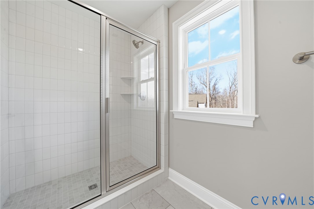 Walk-in shower featuring white tiled walls, a metal-framed glass enclosure, built-in shelving, and a dual-pane window