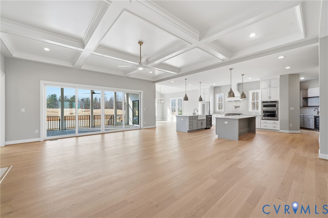 Coffered ceilings with recessed lighting, wood-finish flooring, sliding glass doors, and a kitchen featuring dual islands and built-in stainless steel double ovens
