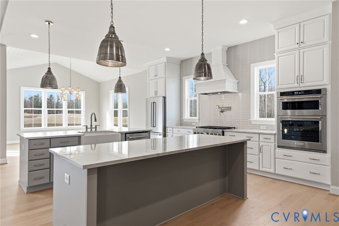 Kitchen featuring white cabinetry, an oversized central island with stone-finish countertops, stainless steel double wall ovens, a farmhouse sink, and pendant lighting