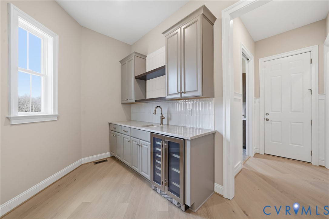 Custom cabinetry with built-in beverage refrigerator, stone-surface countertop, sink with gooseneck faucet, white vertical tile backsplash, and wood-finish flooring