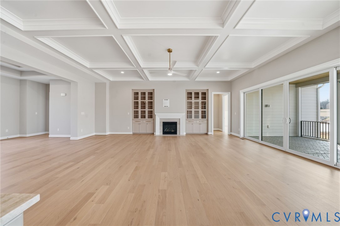 Coffered ceiling, wood-finish flooring, built-in cabinetry, fireplace with a mantle, and multi-panel sliding glass doors