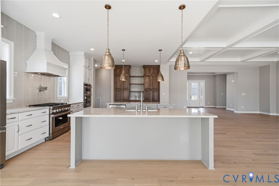 Kitchen featuring a center island with countertop seating, wood-finish flooring, custom cabinetry with integrated stainless steel appliances, a tile backsplash, and coffered ceiling detailing