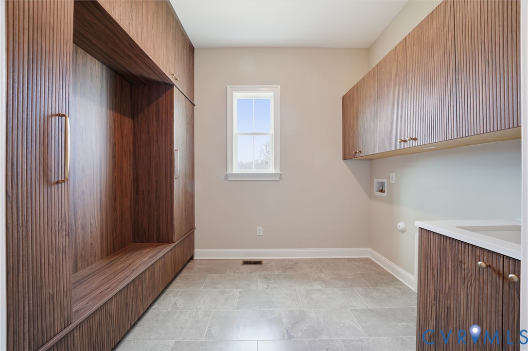 Custom fluted wood-finish cabinetry, stone-composite tile flooring, integrated storage shelving, and a neutral countertop with an under-mount sink