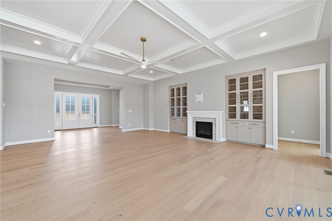 Coffered ceiling, wood-finish flooring, built-in glass-front cabinetry, gas fireplace with decorative mantel, and double-door exterior entry