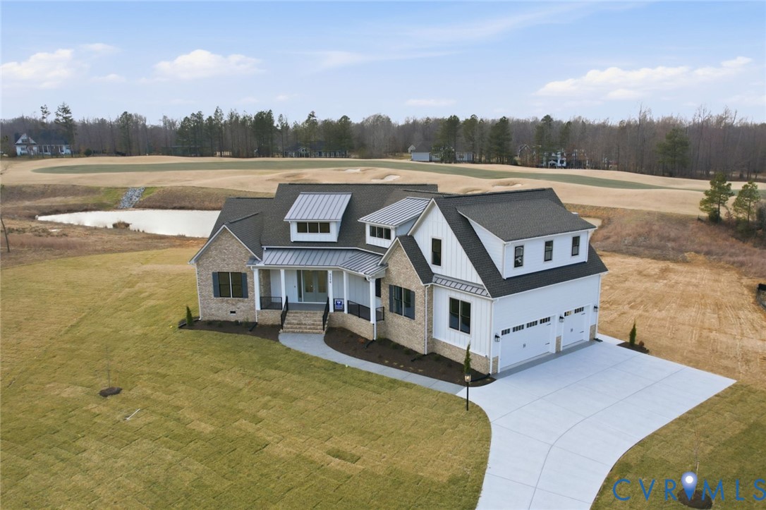 Two-story residence featuring a brick and vertical siding exterior, metal roof accents, covered front porch with iron railing, and attached two-car garage