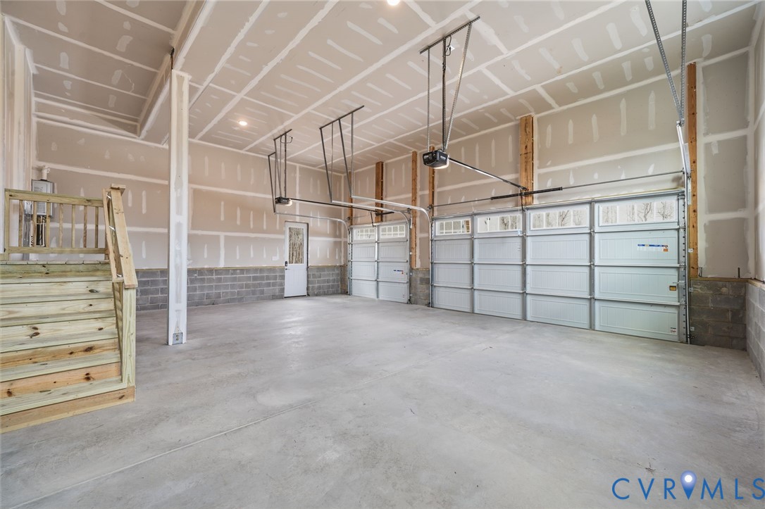 Spacious multi-car garage featuring a smooth concrete floor, high ceilings, automatic roll-up doors, and wooden staircase access